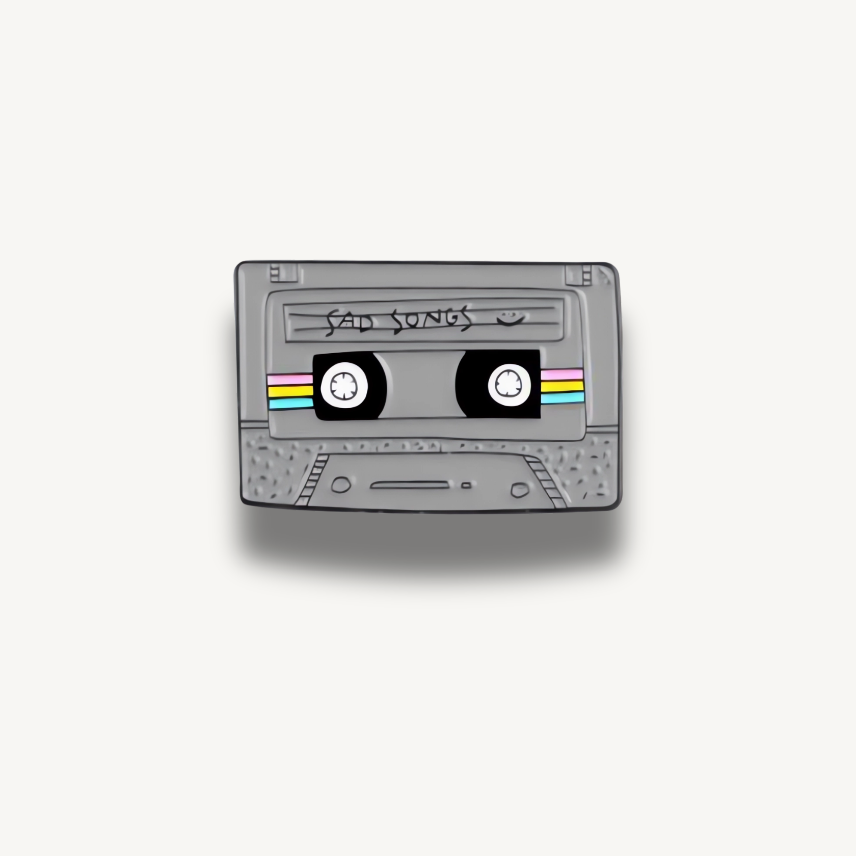 Sivá smaltovaná brošňa v tvare retro kazety s nápisom 'Sad Songs' a farebnými prúžkami.