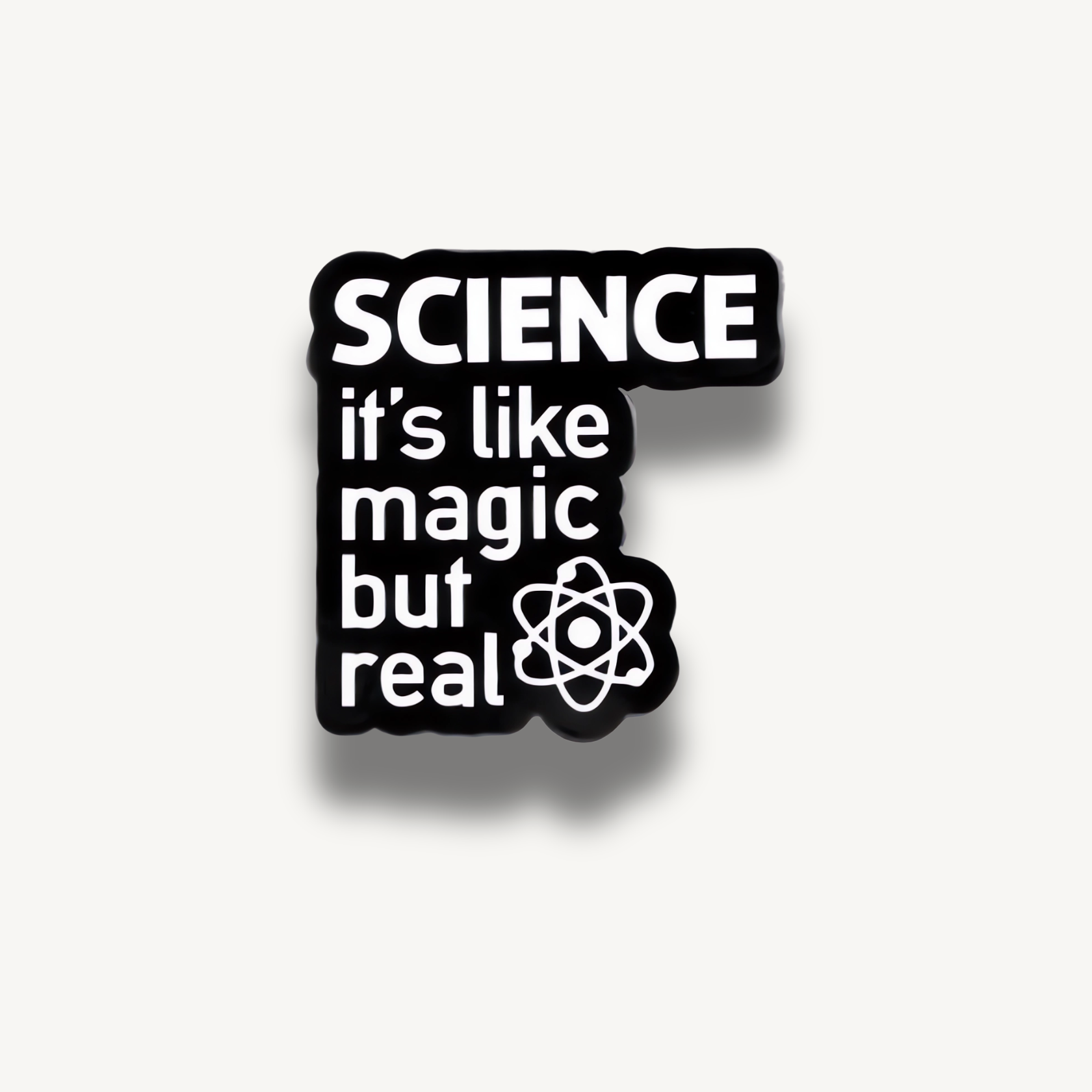 Čierna smaltovaná brošňa s bielym textom 'SCIENCE it's like magic but real' a symbolom atómu.