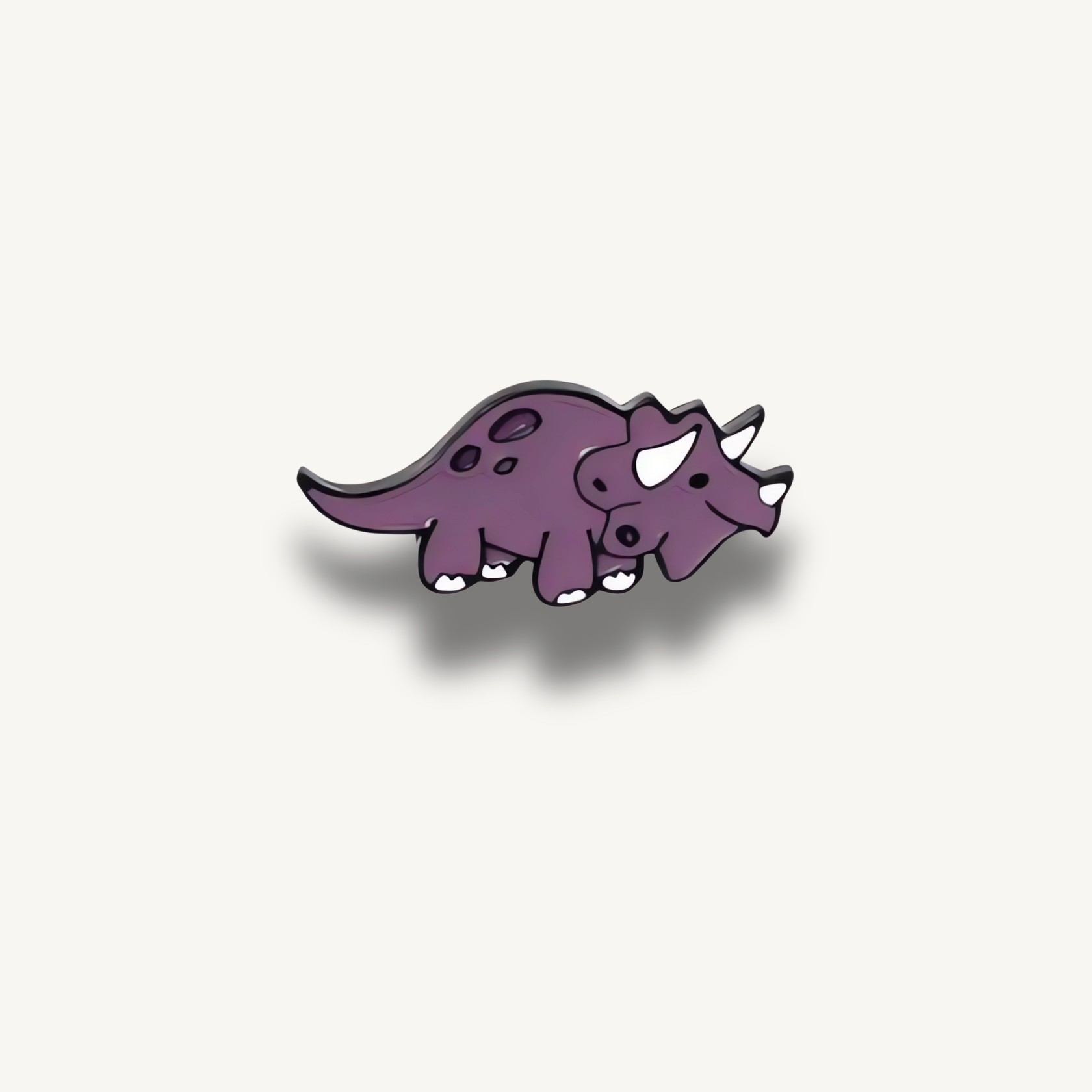 Smaltovaná brošňa fialového dinosaura s tromi rohmi a tmavými škvrnami.