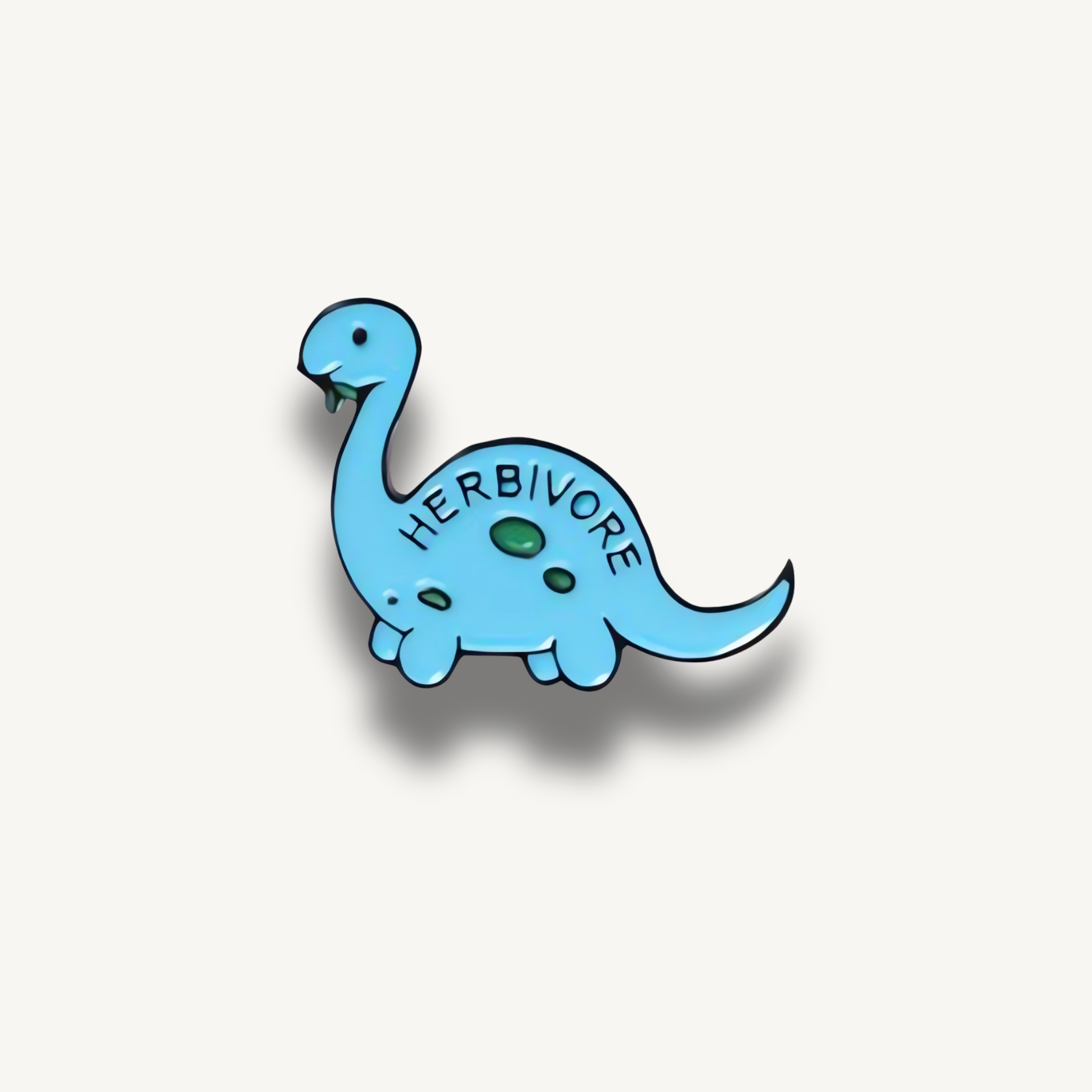 Modrá brošňa s kresleným dinosaurom a nápisom Herbivore so zeleným listom v ústach.