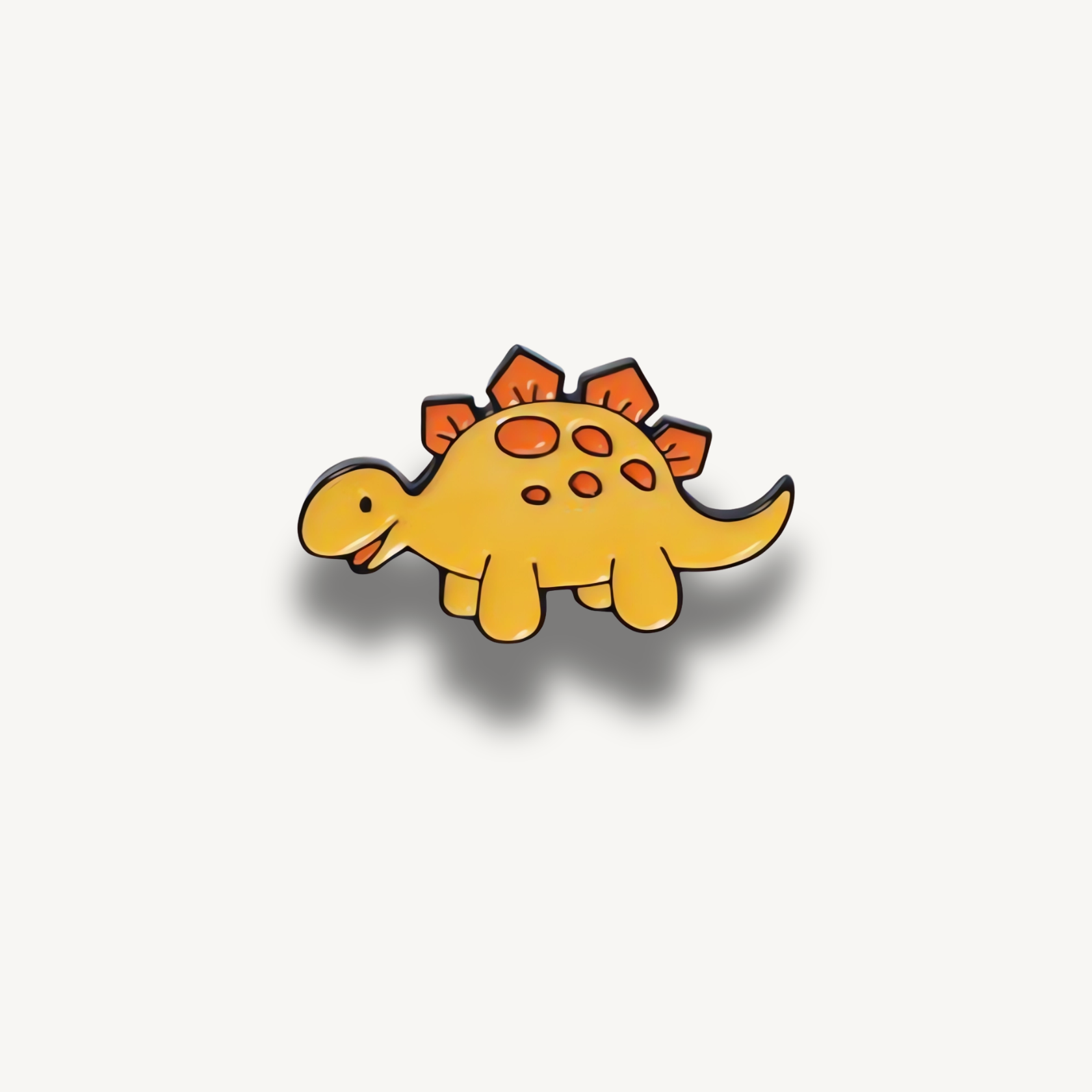 Žltá brošňa dinosaura s oranžovými platničkami na chrbte a bodkami.