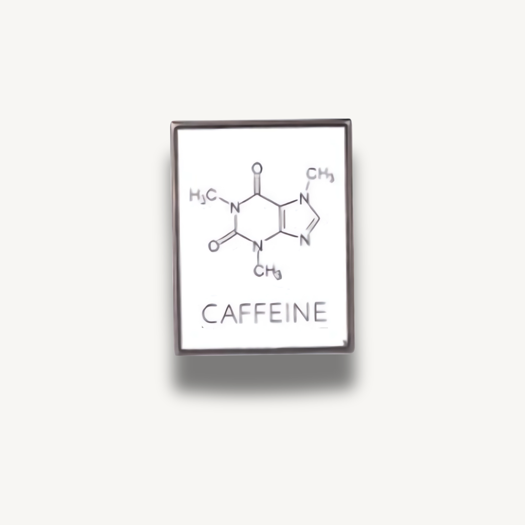 Biela smaltovaná brošňa s chemickou štruktúrou kofeínu a nápisom CAFFEINE.