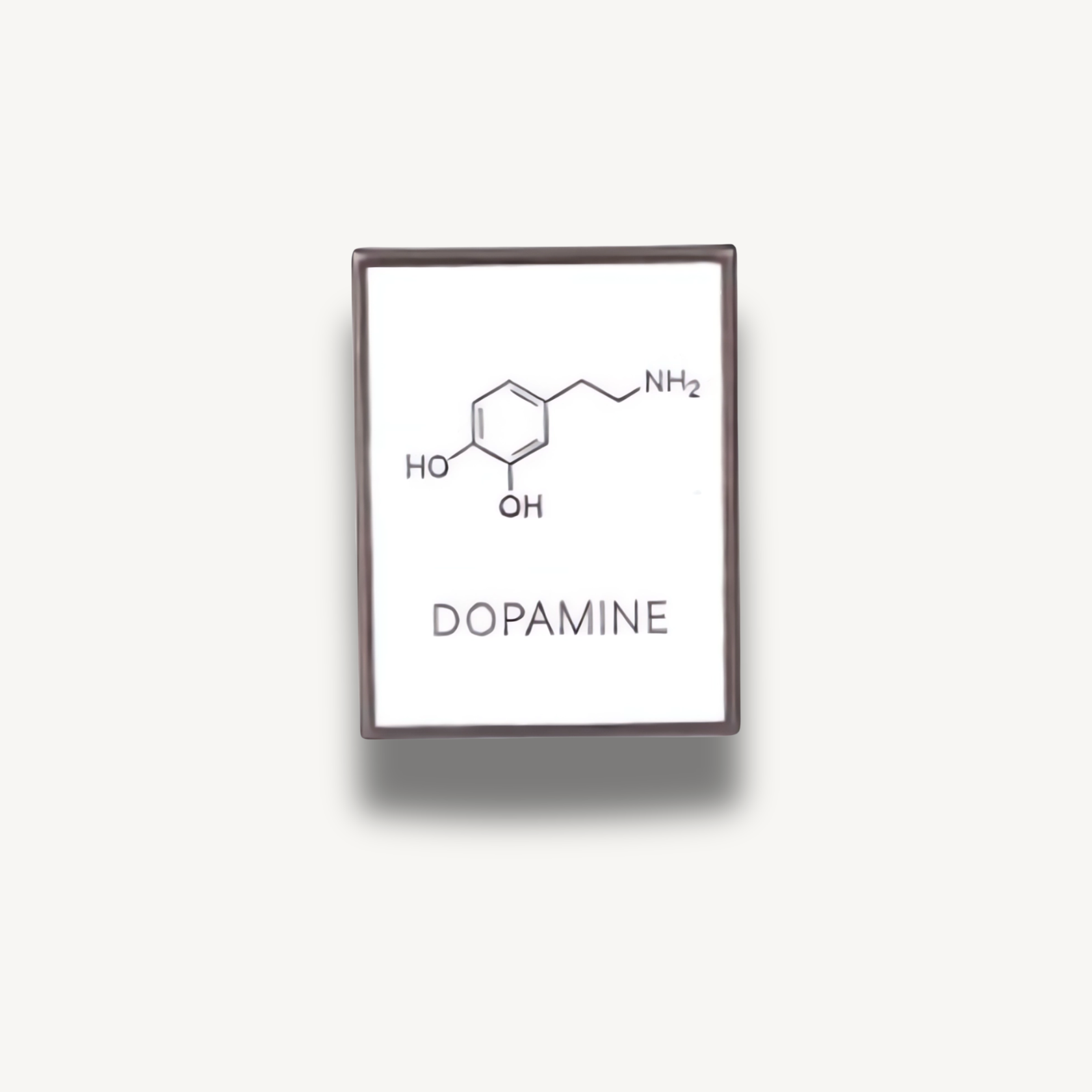 Strieborná brošňa s bielym podkladom zobrazujúca čierny chemický vzorec dopamínu s nápisom DOPAMINE.