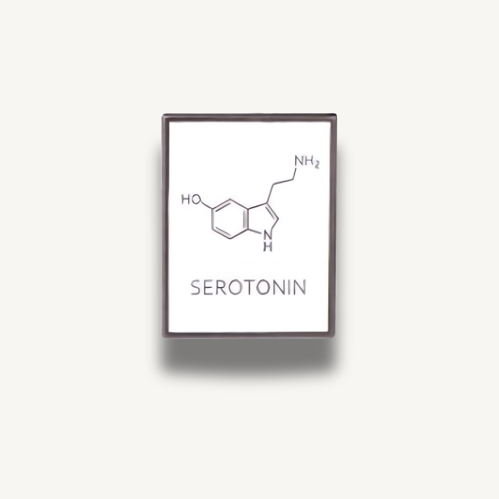 Biely obdĺžnikový brošňa s chemickým vzorcom serotonínu a nápisom serotonín.