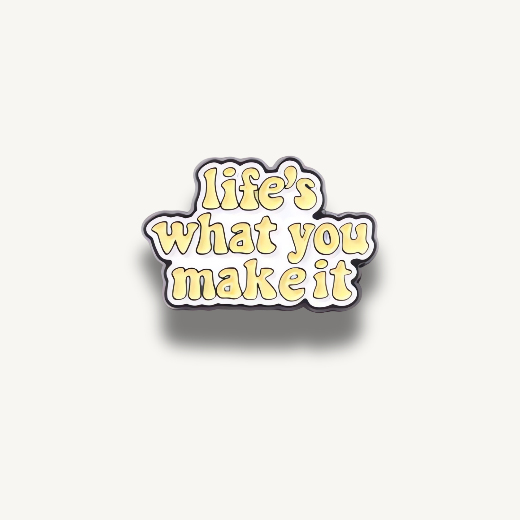 Smaltovaná brošňa s bublinkovým žltým nápisom „life's what you make it“ na bielom pozadí s čiernym obrysom.