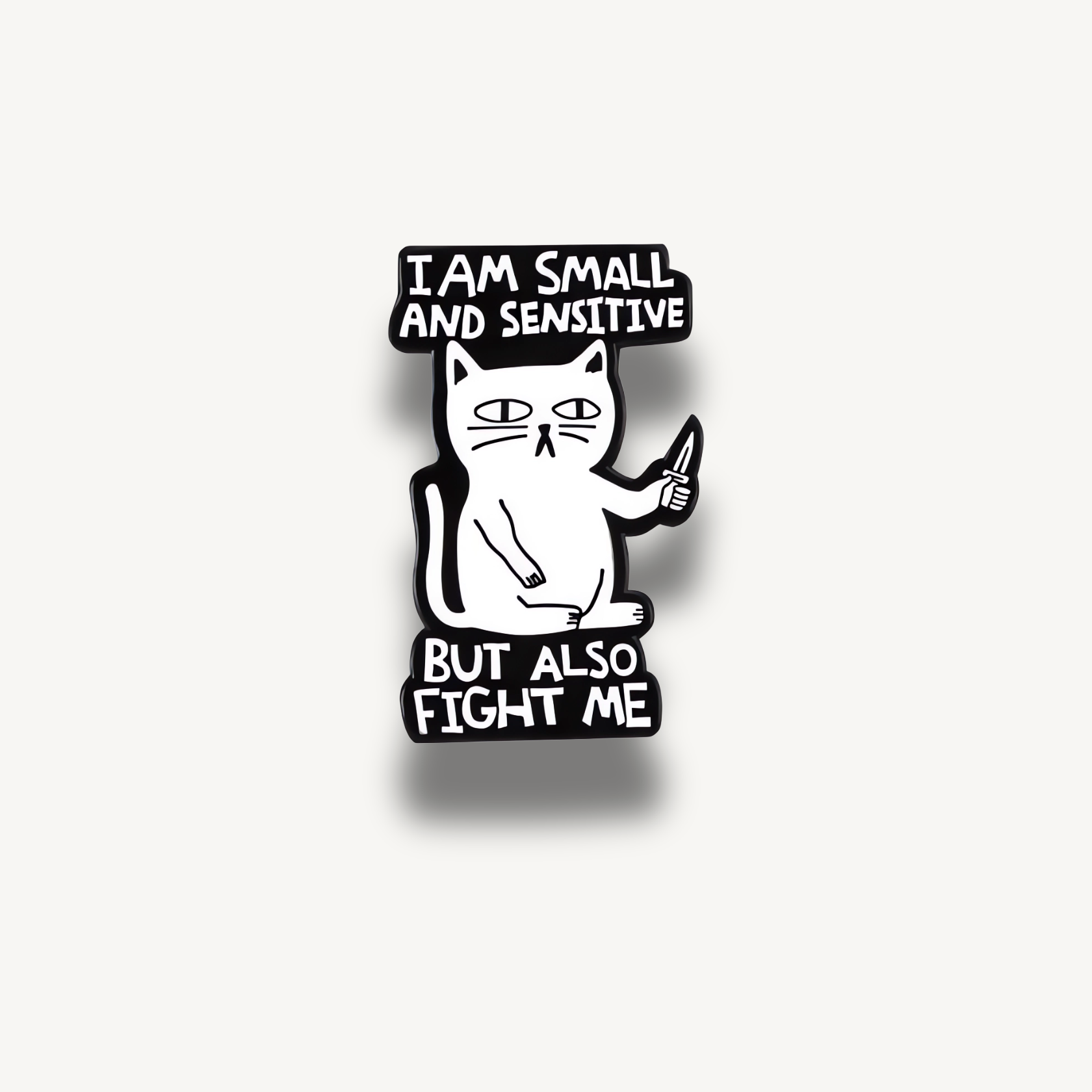 Brošňa s bielou mačkou držiaca nôž a nápisy: I AM SMALL AND SENSITIVE BUT ALSO FIGHT ME.