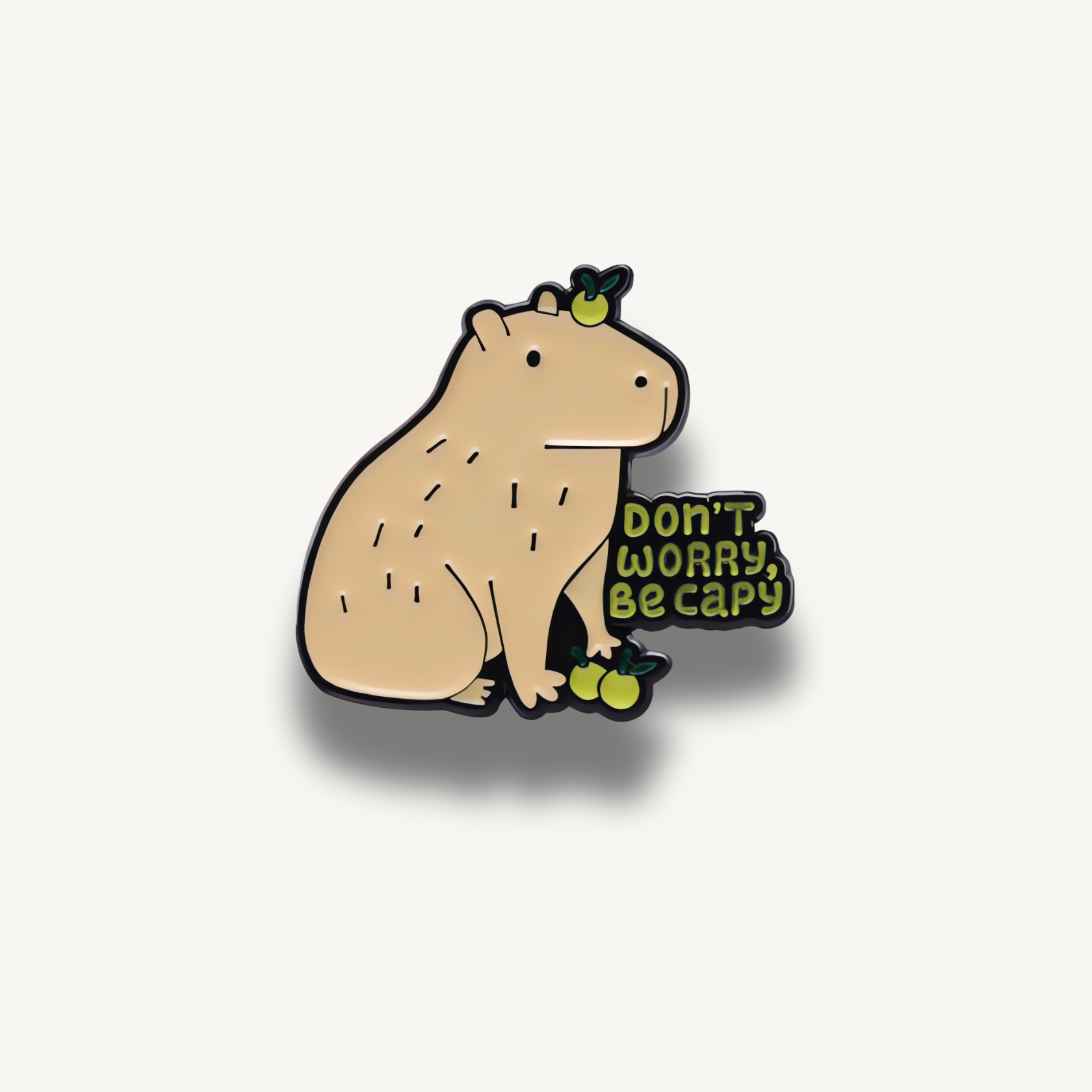 Smaltovaná brošňa s kapybarou a nápisom 'Don't Worry, Be Capy' so zelenými plodmi.