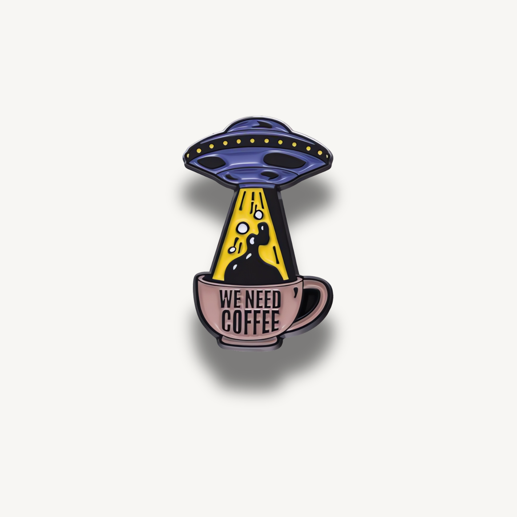 Brošňa s fialovým lietajúcim tanierom unášajúcim čiernu kávu z hnedého hrnčeka s nápisom 'WE NEED COFFEE'.