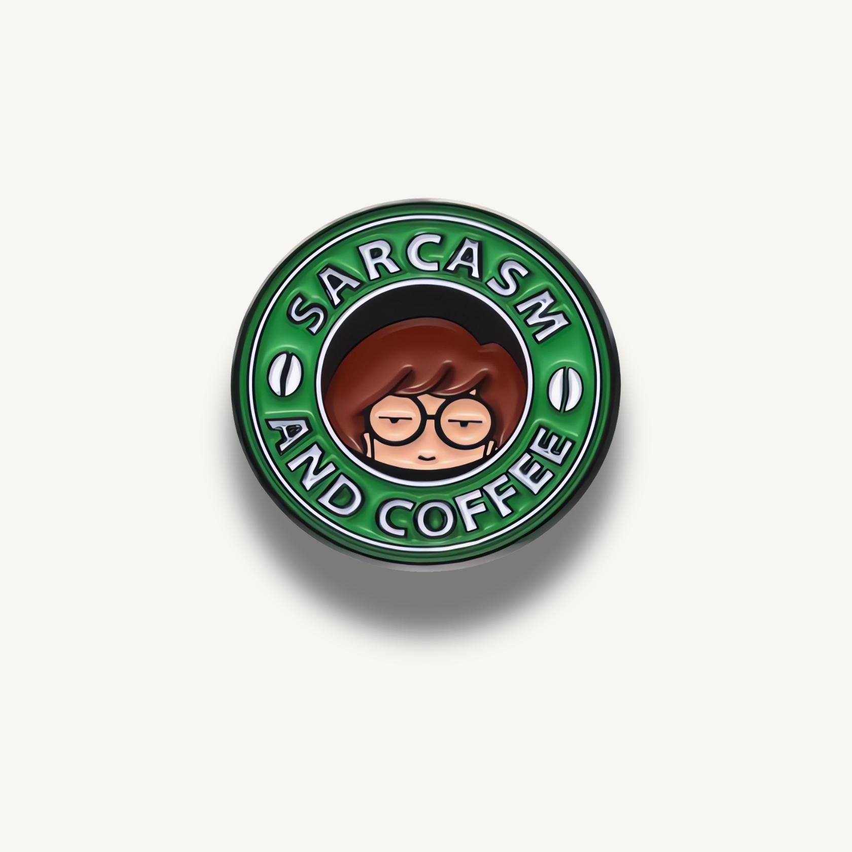 Zelená kruhová brošňa s hnedovlasou postavičkou v okuliaroch a nápisom Sarcasm and Coffee.