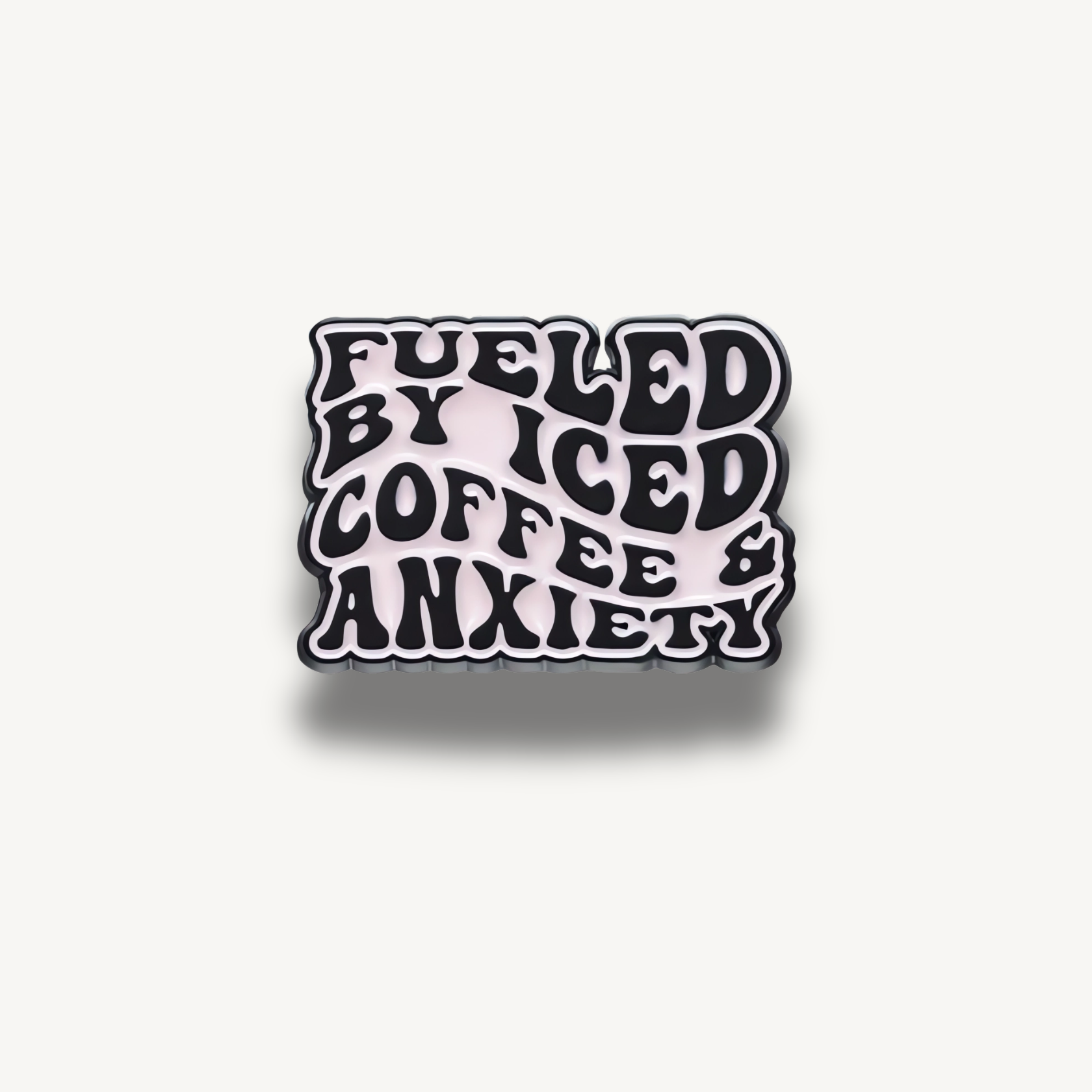 Smaltovaná brošňa s čiernym vlnitým textom 'Fueled by Iced Coffee & Anxiety' na svetloružovom pozadí.