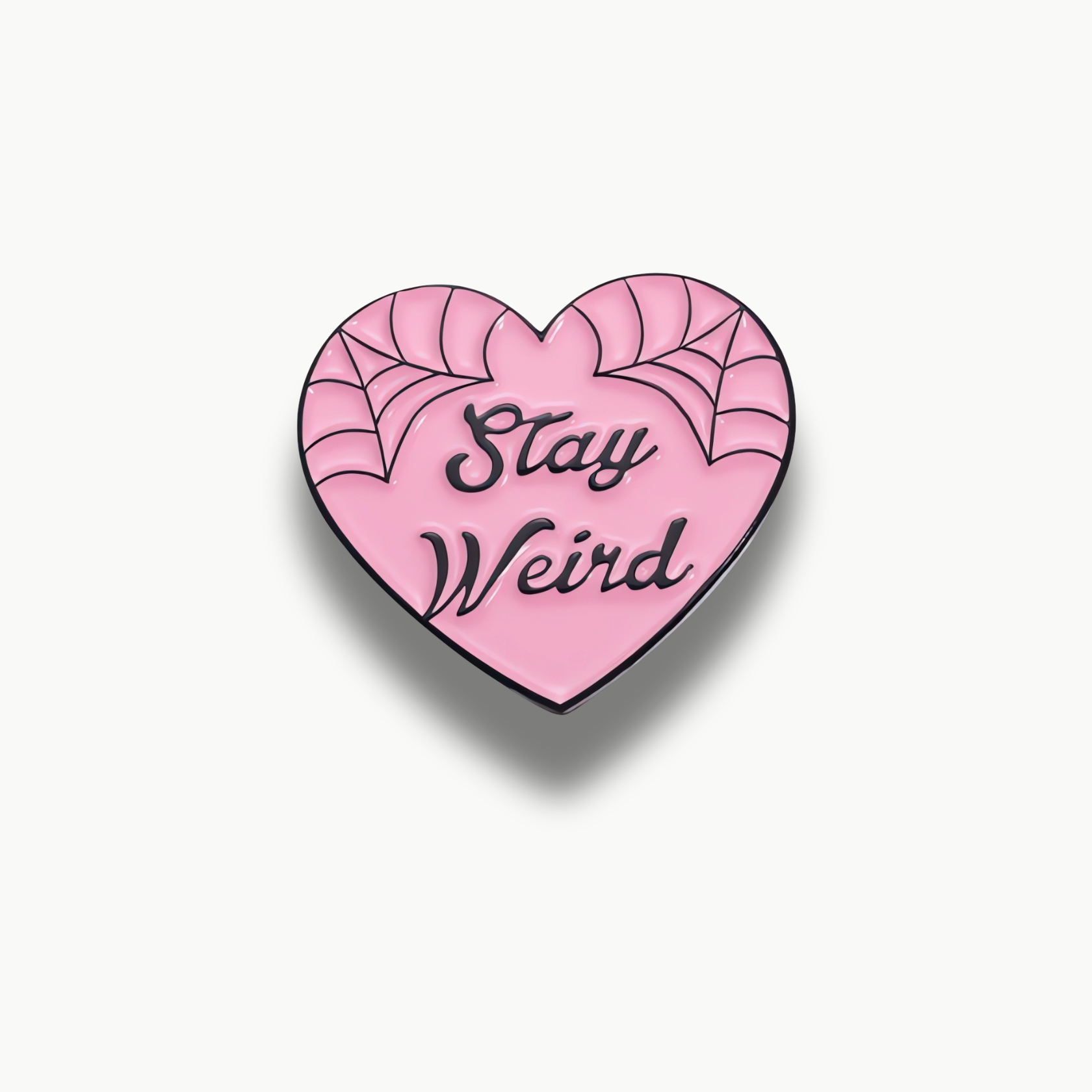 Ružová brošňa v tvare srdca s čiernymi pavučinami a nápisom Stay Weird.