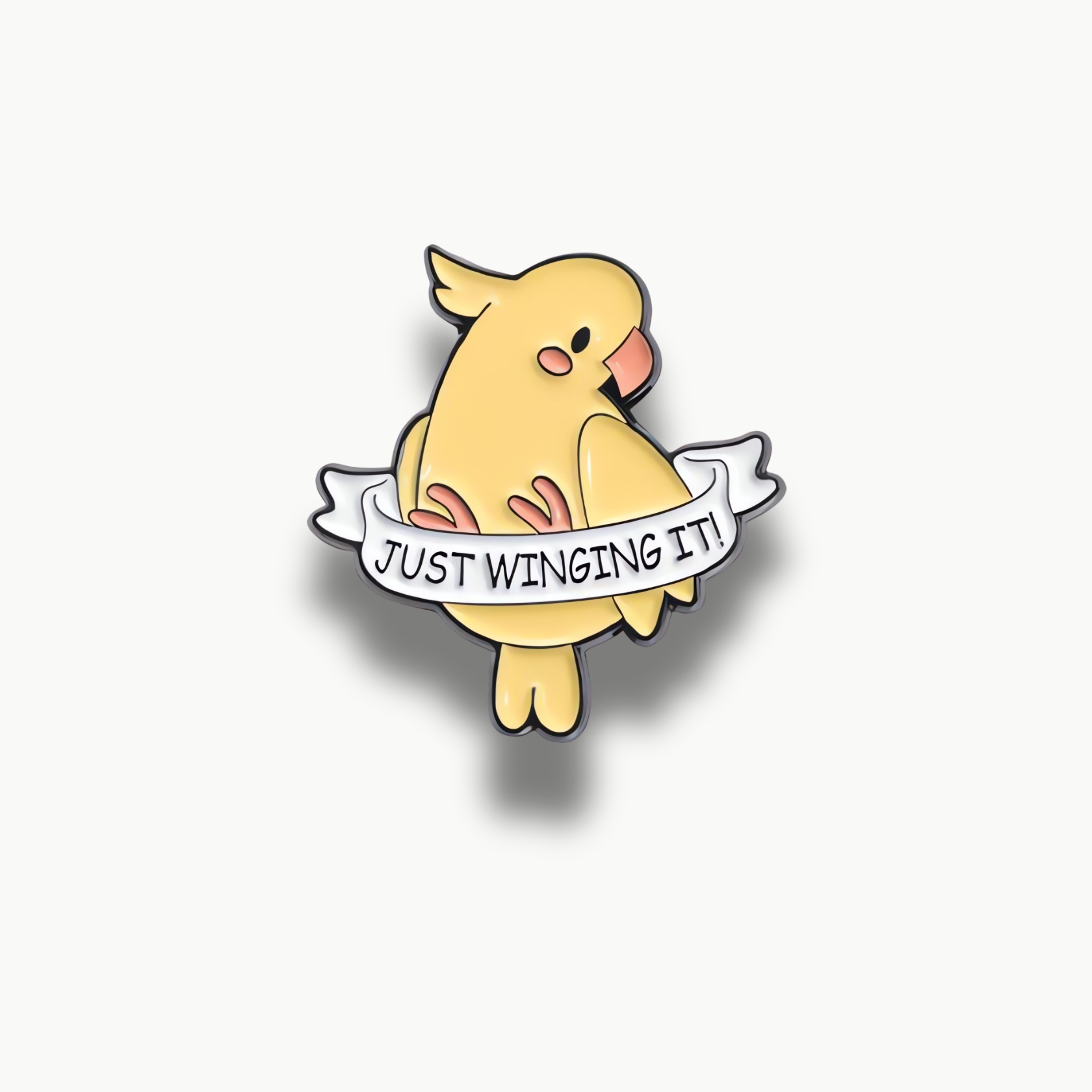 Brošňa zobrazujúca žltého vtáčika s bielym transparentom a nápisom "Just Winging It!".