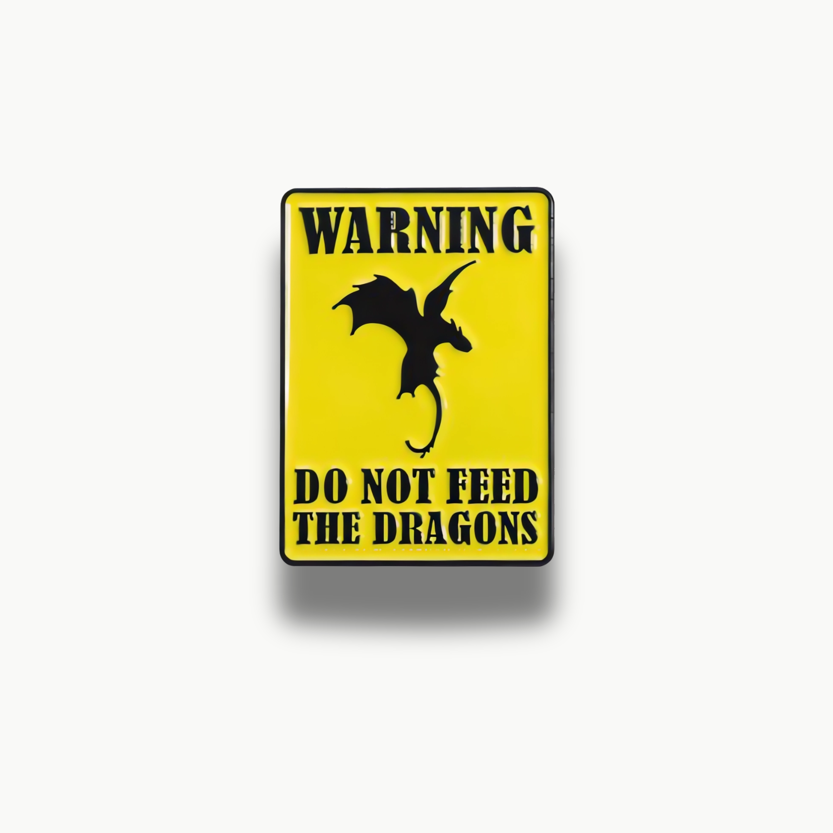 Žltá obdĺžniková brošňa s čiernym nápisom 'WARNING DO NOT FEED THE DRAGONS' a siluetou draka.