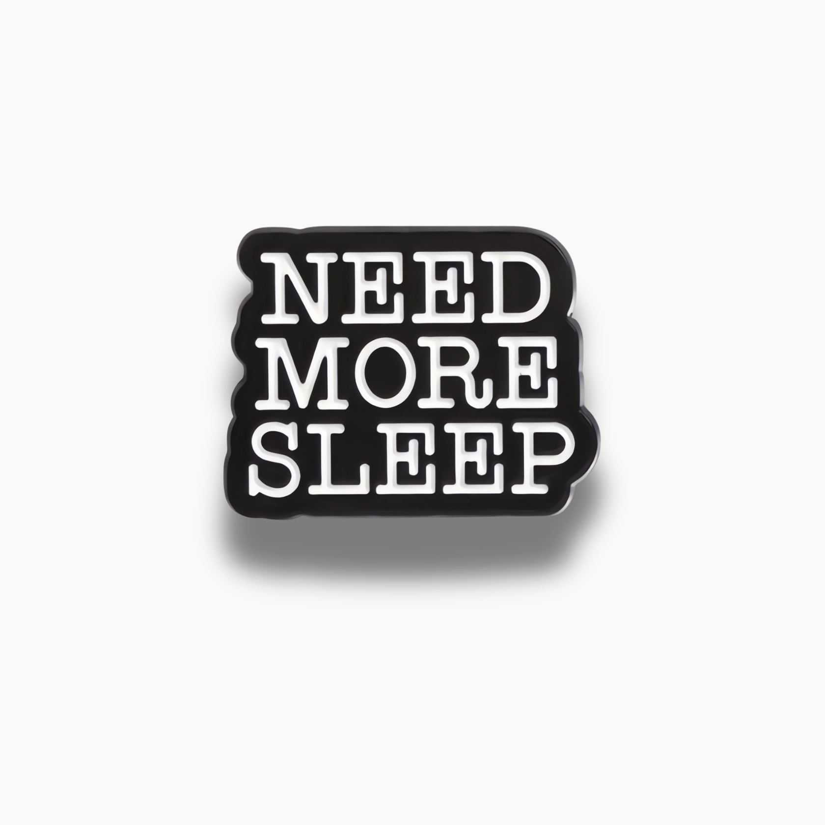 Smaltovaná brošňa s čiernym pozadím a bielym textom 'Need More Sleep'.
