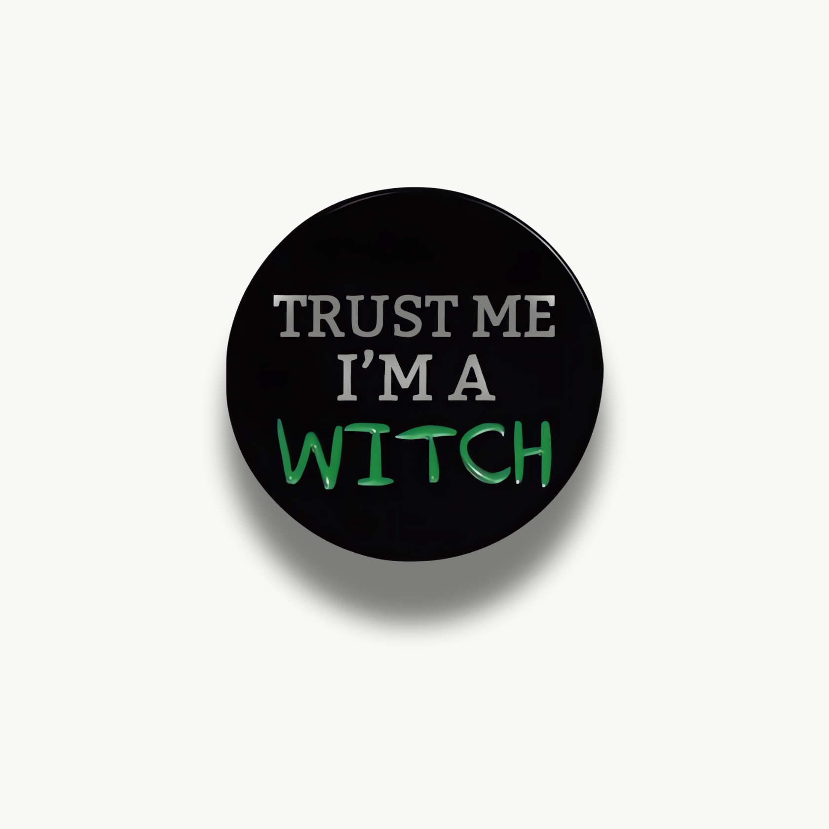 Čierna kruhová brošňa s bielym a zeleným nápisom "Trust Me I'm A Witch".