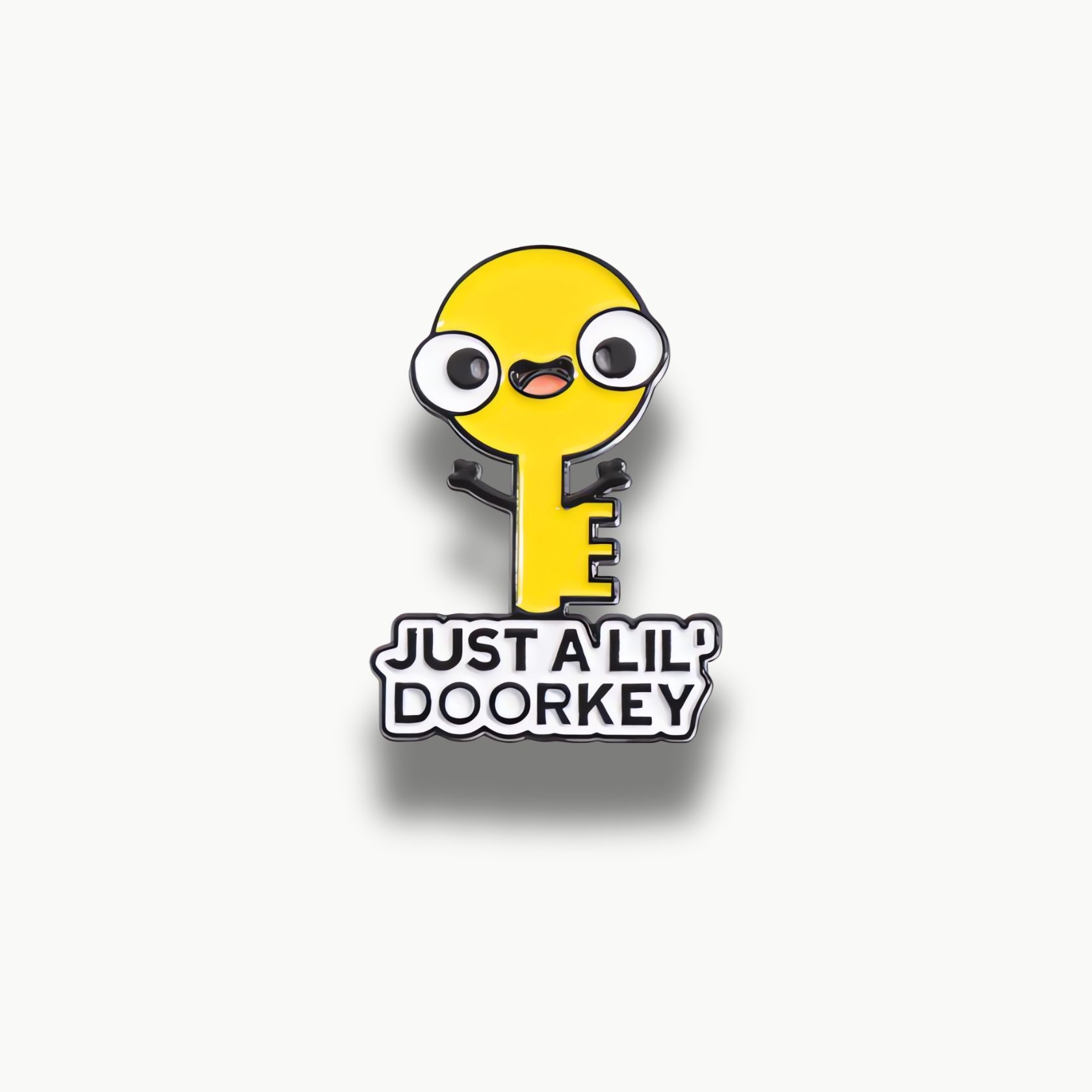 Žltá brošňa v tvare kľúča s kreslenou tvárou, očami a nápisom 'Just a lil' doorkey'.