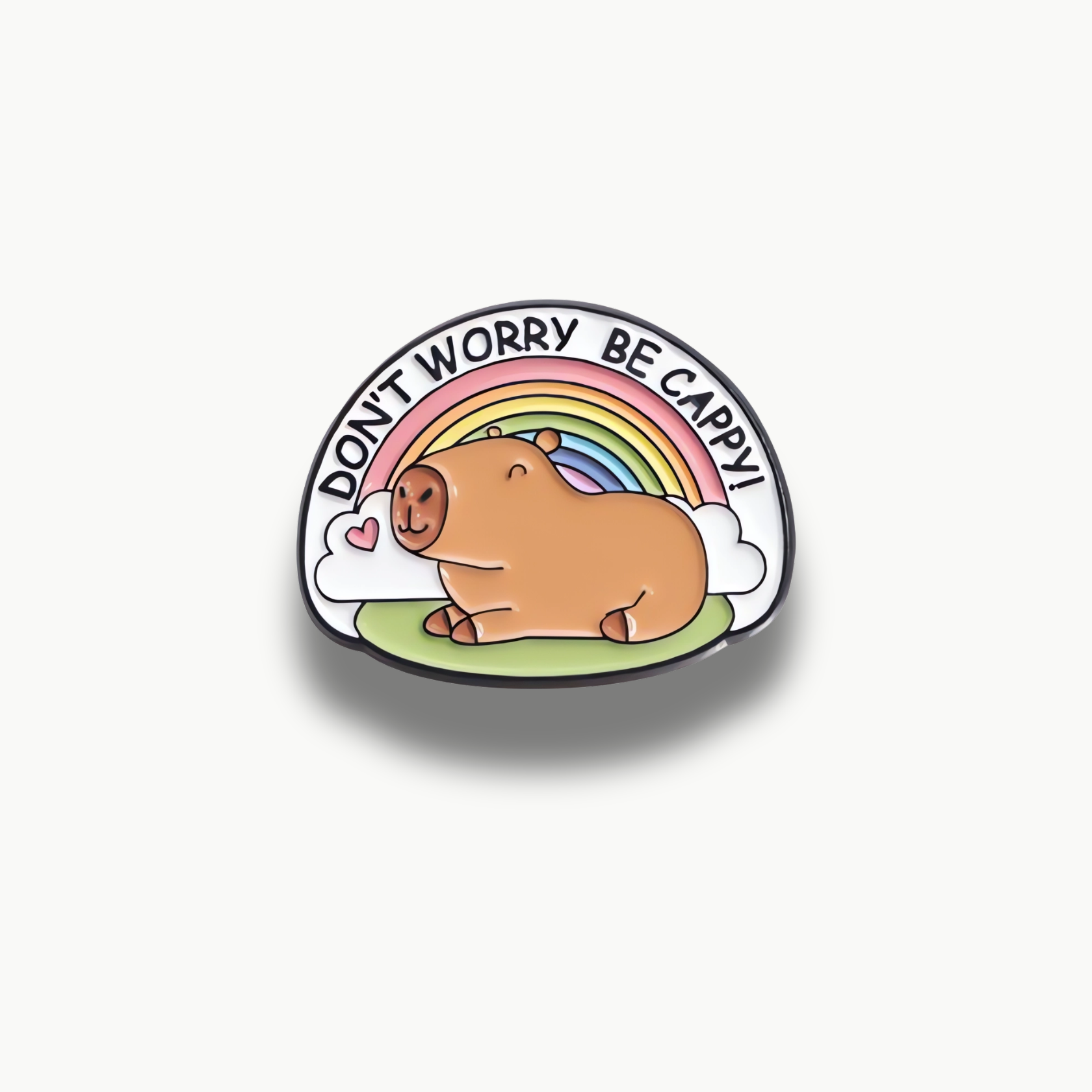 Smaltovaná brošňa s kreslenou kapybarou sediacou na tráve pod farebnou dúhou s textom "DON'T WORRY BE CAPPY!".