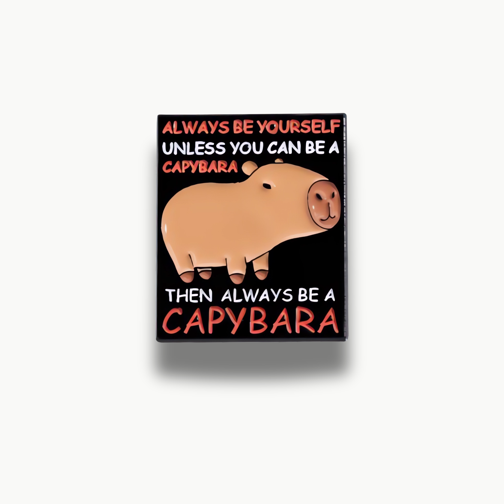 Smaltovaná brošňa s hnedou kapybarou na čiernom pozadí a bielym a oranžovým nápisom 'Always be yourself unless you can be a capybara, then always be a capybara'.