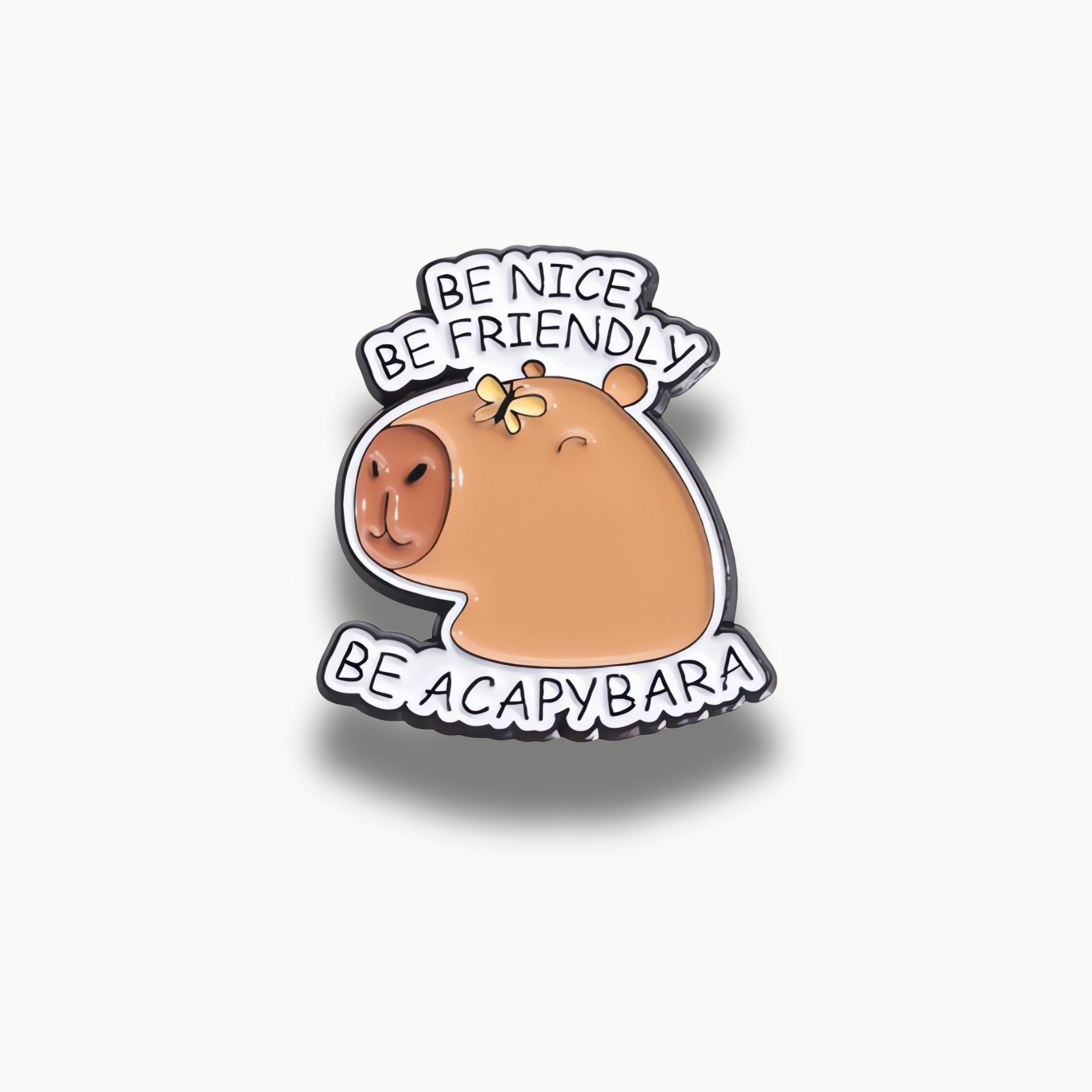 Smaltovaná brošňa s kreslenou hnedou kapybarou, malým žltým motýľom a nápisom "BE NICE BE FRIENDLY BE ACAPYBARA".