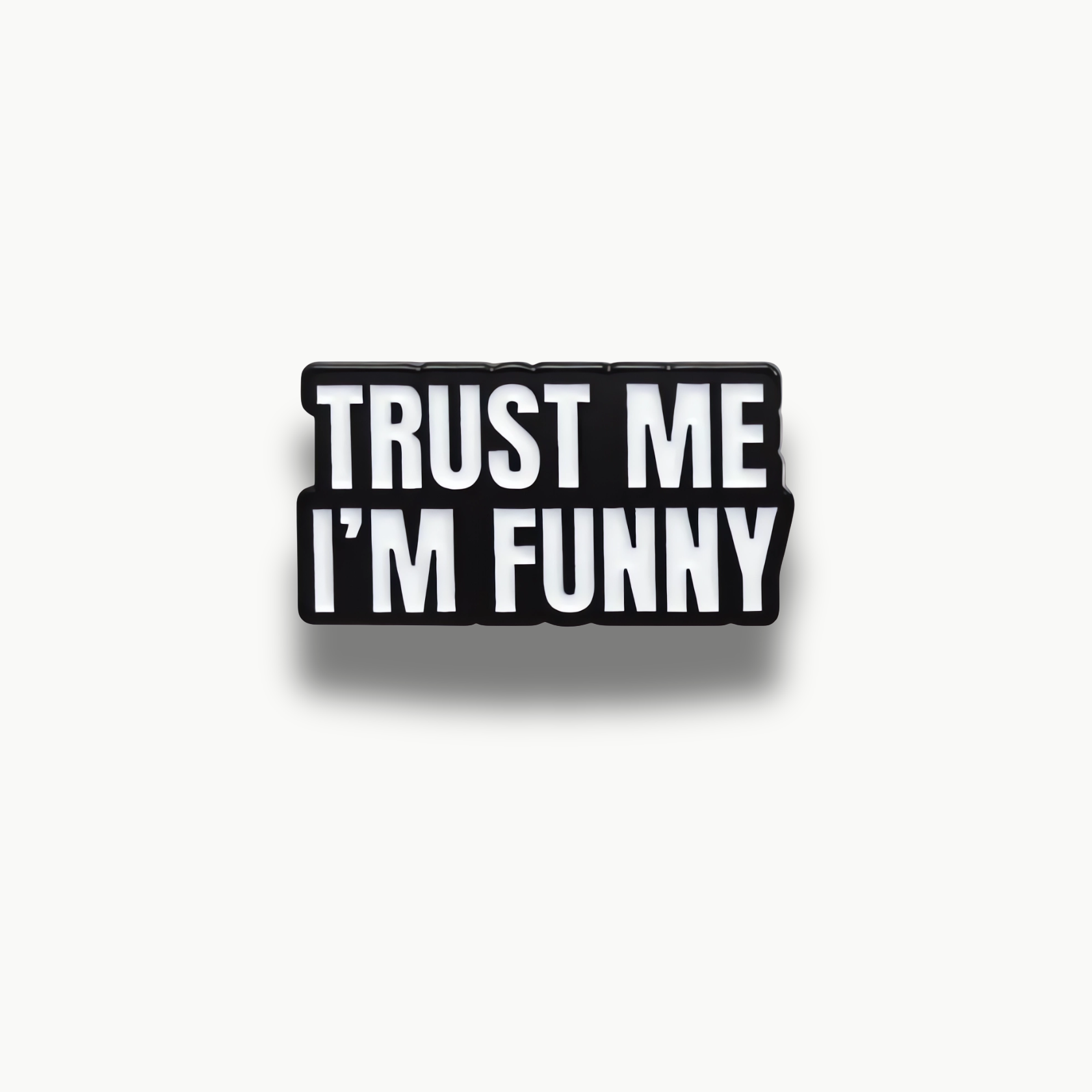 Čierna smaltovaná brošňa s bielym nápisom 'Trust Me I'm Funny'.