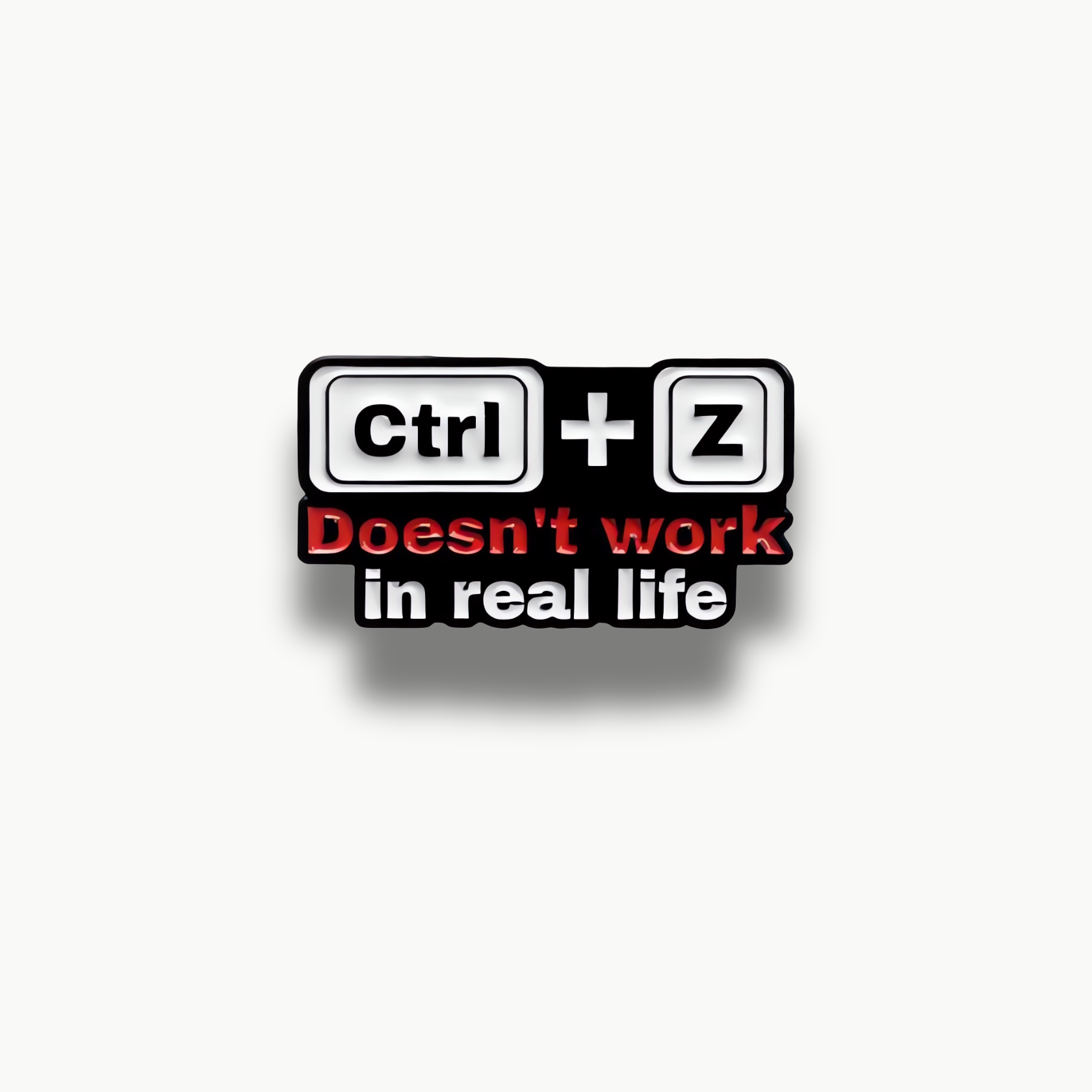 Brošňa s čiernymi klávesami Ctrl a Z a červeno-bielym nápisom "Doesn't work in real life".