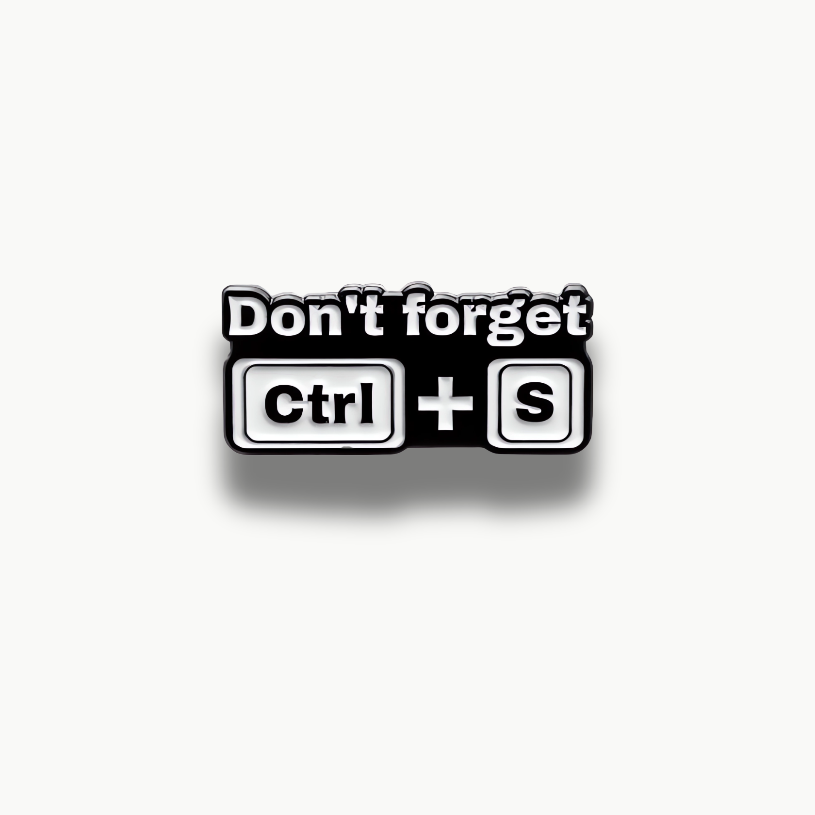 Čierno-biela smaltovaná brošňa s textom "Don't forget" a klávesovými skratkami Ctrl + S.