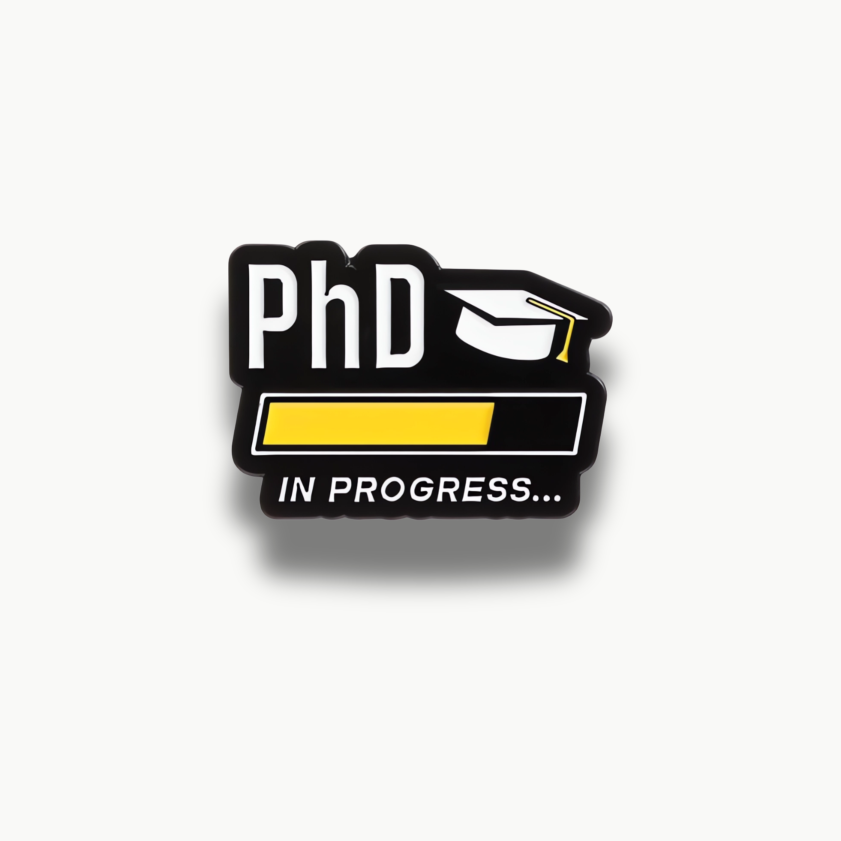 Smaltovaná brošňa s nápisom PhD, promóčnou čiapkou a indikátorom načítania 'in progress' na čiernom pozadí.